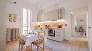 Una cocina moderna con armarios blancos, horno empotrado y comedor con mesa para cuatro.