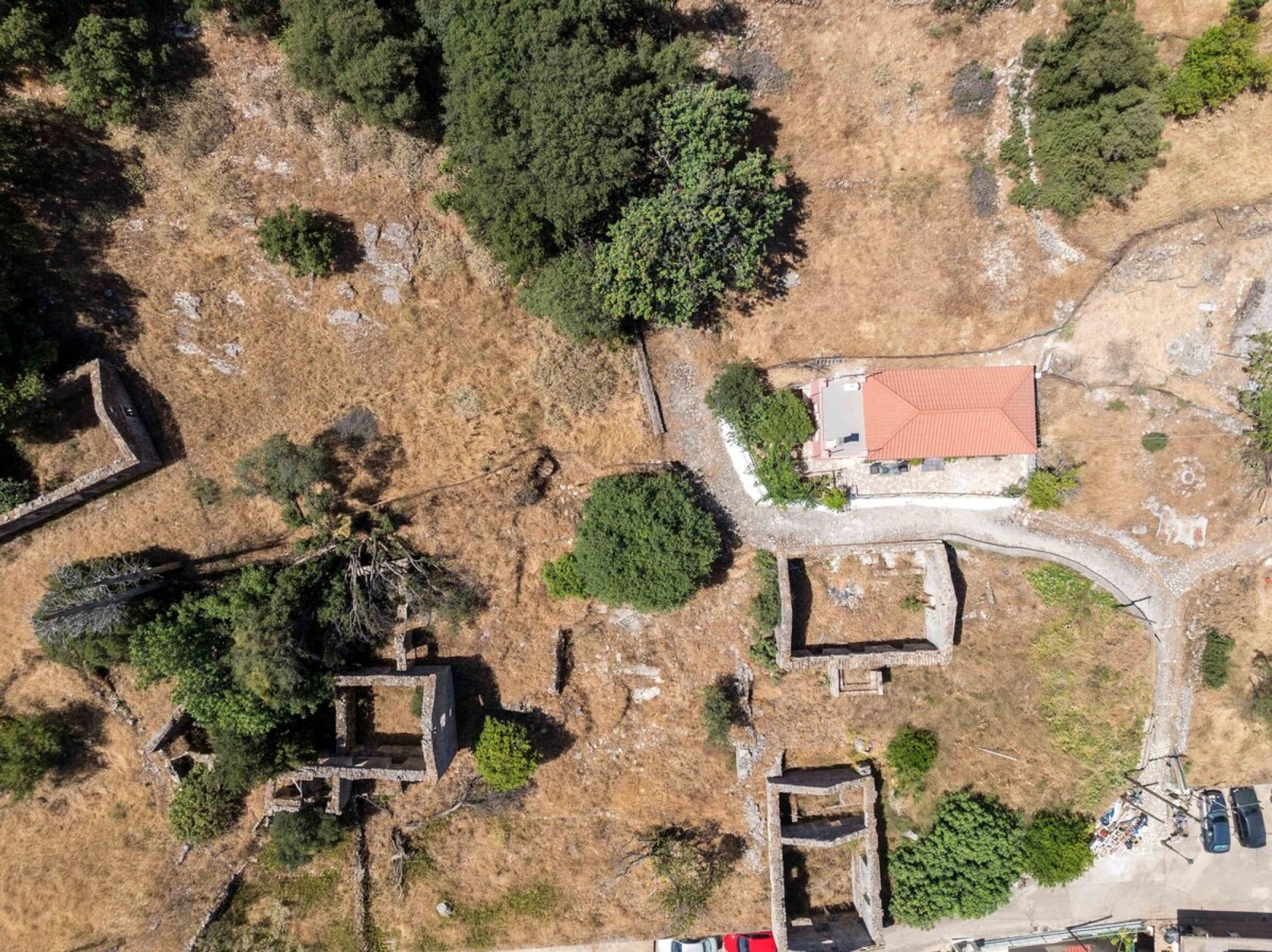 An aerial view of a historical site with ruins, a red-roofed building, and surrounding vegetation.