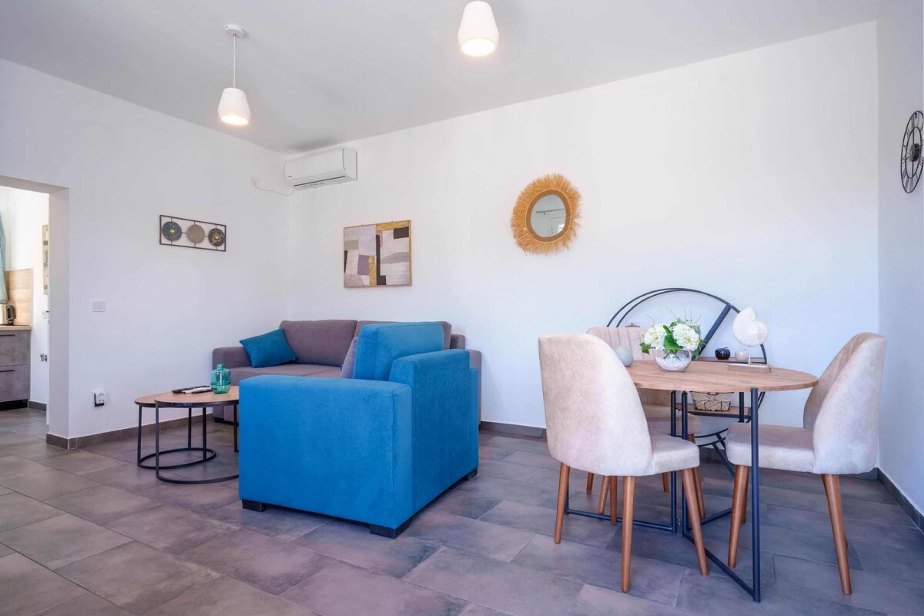 A modern living room with a blue sofa, a small table, and a dining area with chairs.