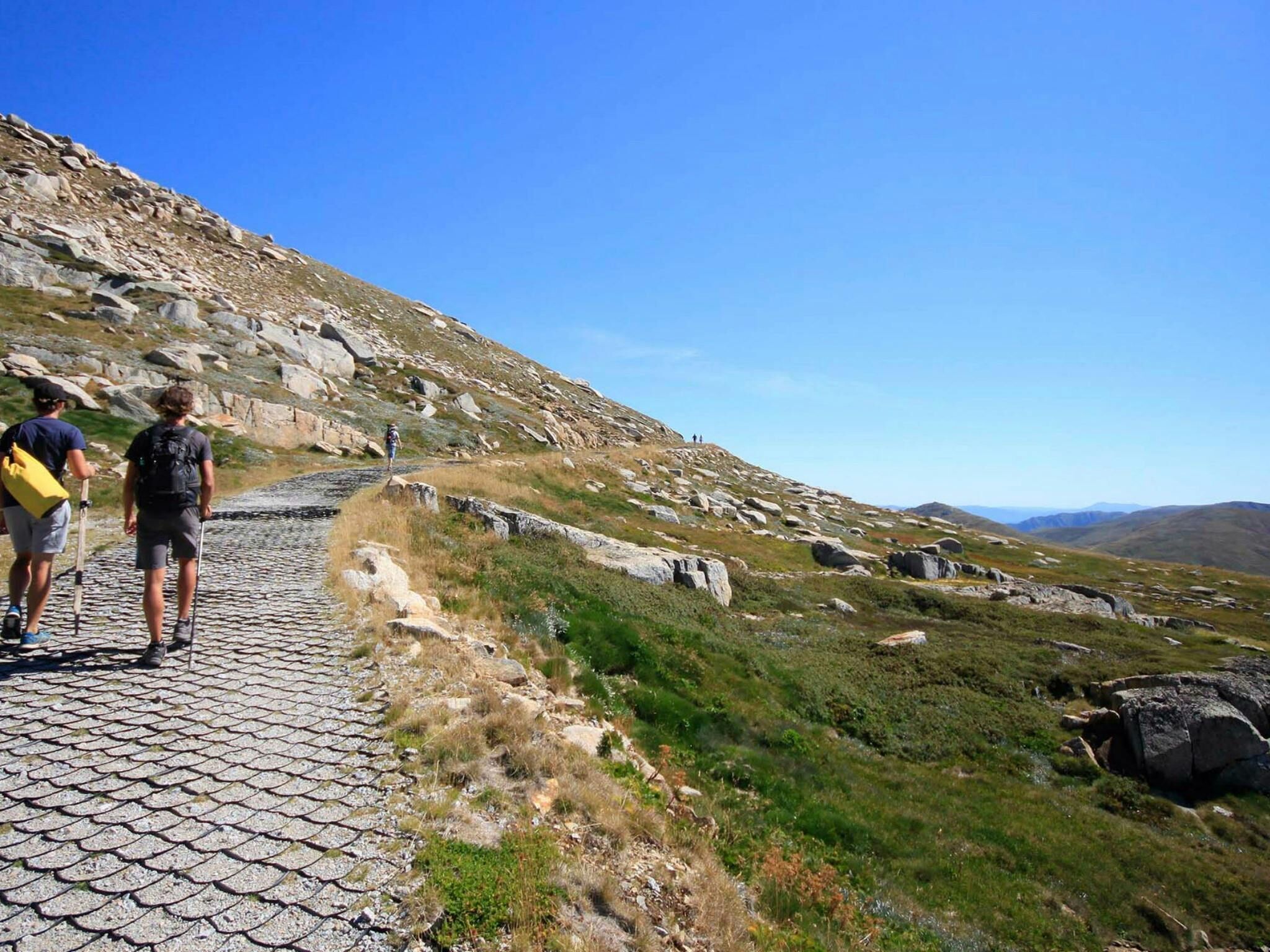 Ein Steinweg auf einer Hügelkuppe, Wanderer sind unterwegs.
