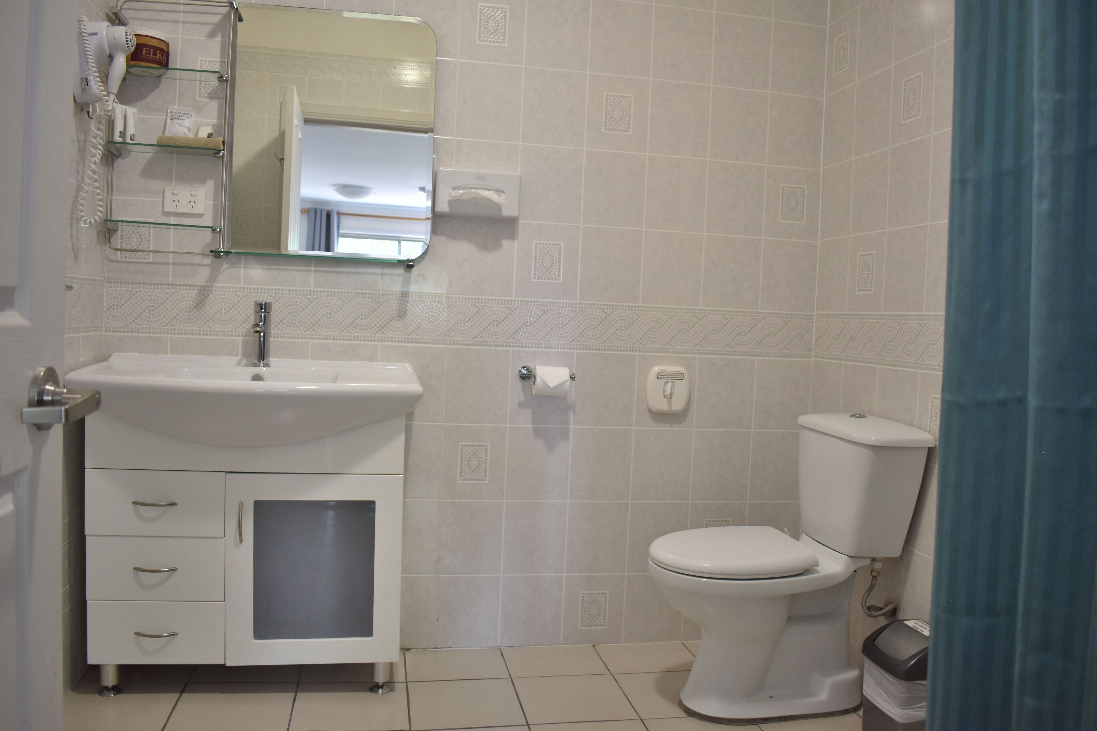 Casa de banho com lavatório branco, espelho, sanita e um contentor de lixo.