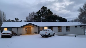 A modern house with a garage, a driveway, and a car parked in the snow. - san michele resort (Adaminaby)