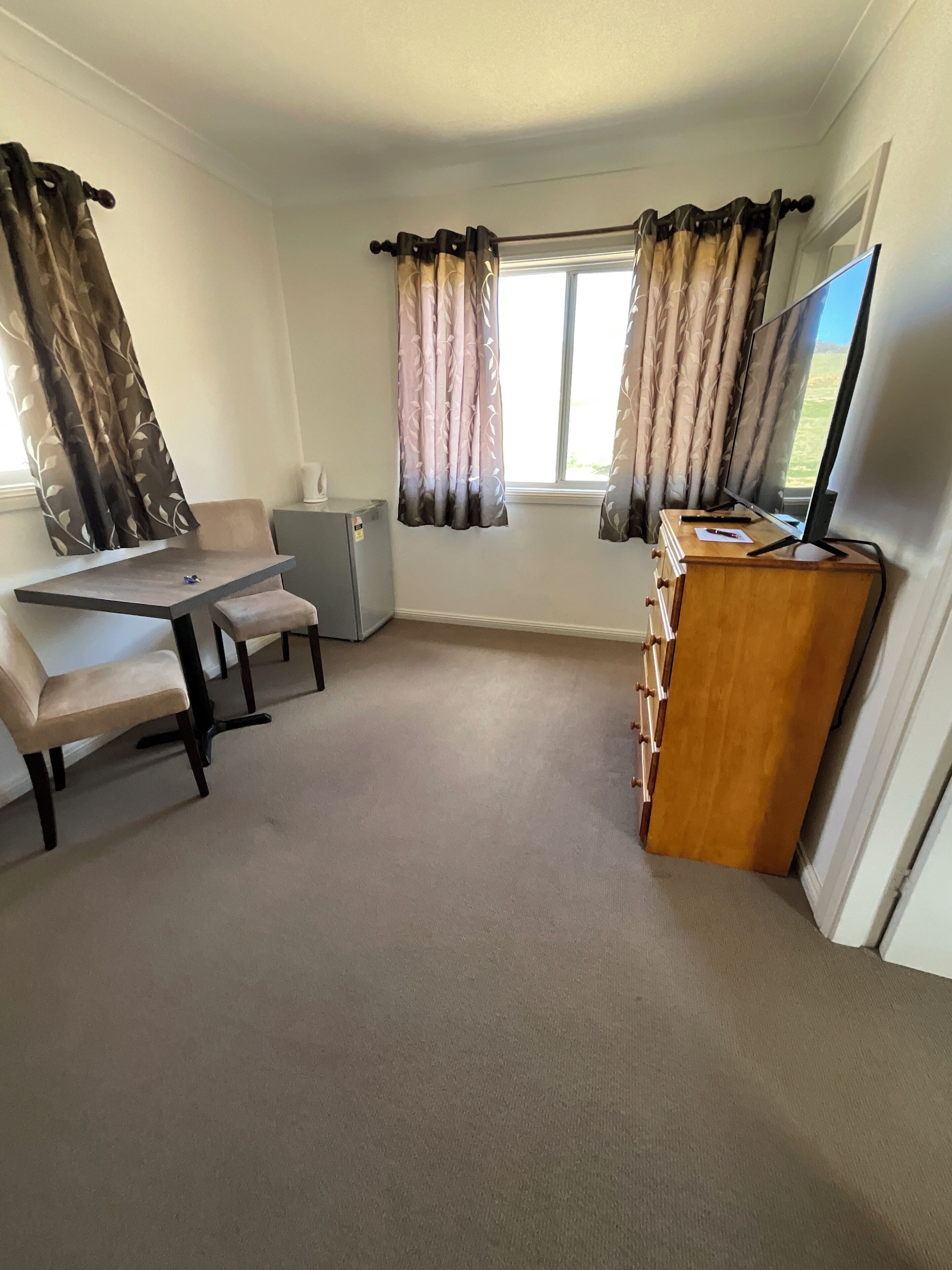 A compact room with a desk, chair, and a television on a wooden stand.