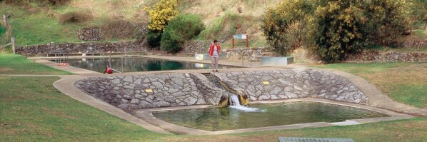A natural pool with a waterfall, surrounded by stone walls and a grassy area. - san michele resort (Adaminaby)