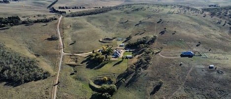 Vista aérea de una propiedad rural con una construcción principal, varias estructuras más pequeñas y un amplio campo abierto.