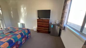 Une chambre d’hôtel équipée d’un lit, d’une commode, d’une télévision, d’un réfrigérateur et d’une fenêtre avec des rideaux.