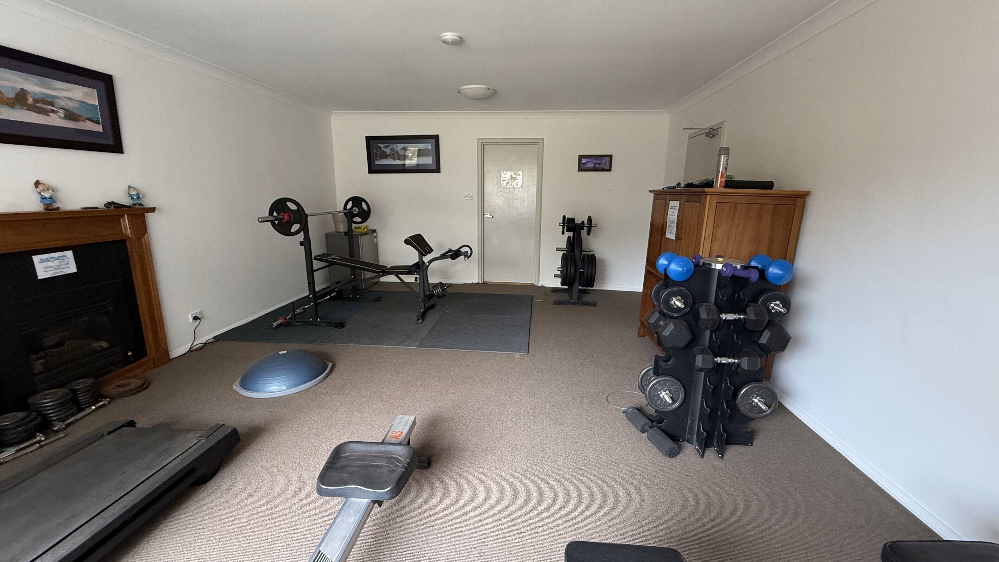 Un gimnasio en casa con una prensa de banca, mancuernas, una estructura para sentadillas y una cinta de correr.