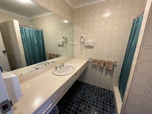 A bathroom with a white sink, a mirror, a towel rack with towels, and a shower with a blue curtain. - san michele resort (Adaminaby)