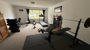 A home gym with exercise equipment, a treadmill, and a window with curtains. - san michele resort (Adaminaby)