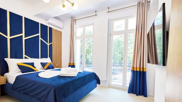 A modern hotel room with a large bed, a TV, and a balcony with curtains. - Carol Park View (Bucharest)