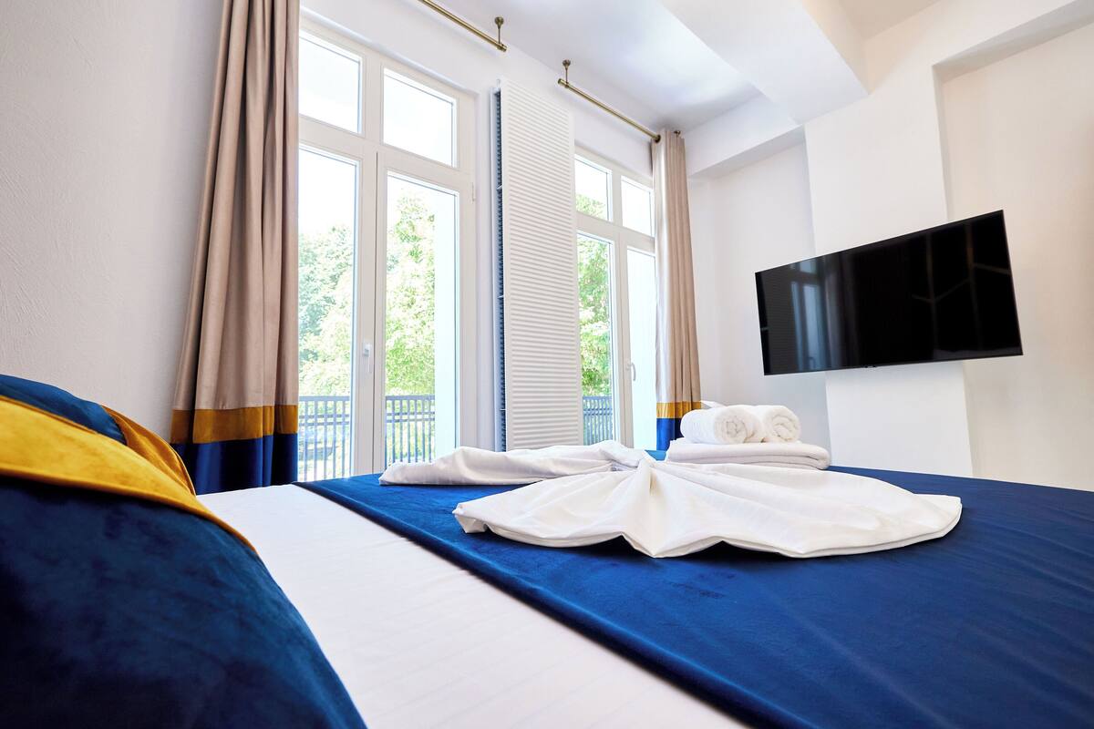 A hotel room with a bed, a TV mounted on the wall, and a window with curtains.