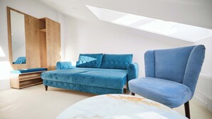 A modern bedroom with a skylight, a blue sofa, a matching armchair, and a large mirror. - Carol Park View (Bucharest)