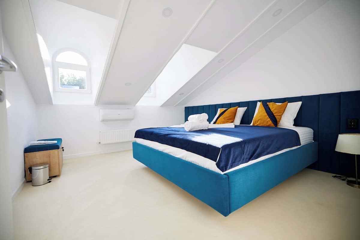 A modern bedroom with a skylight, a bed with blue bedding, and a bedside table with a lamp.
