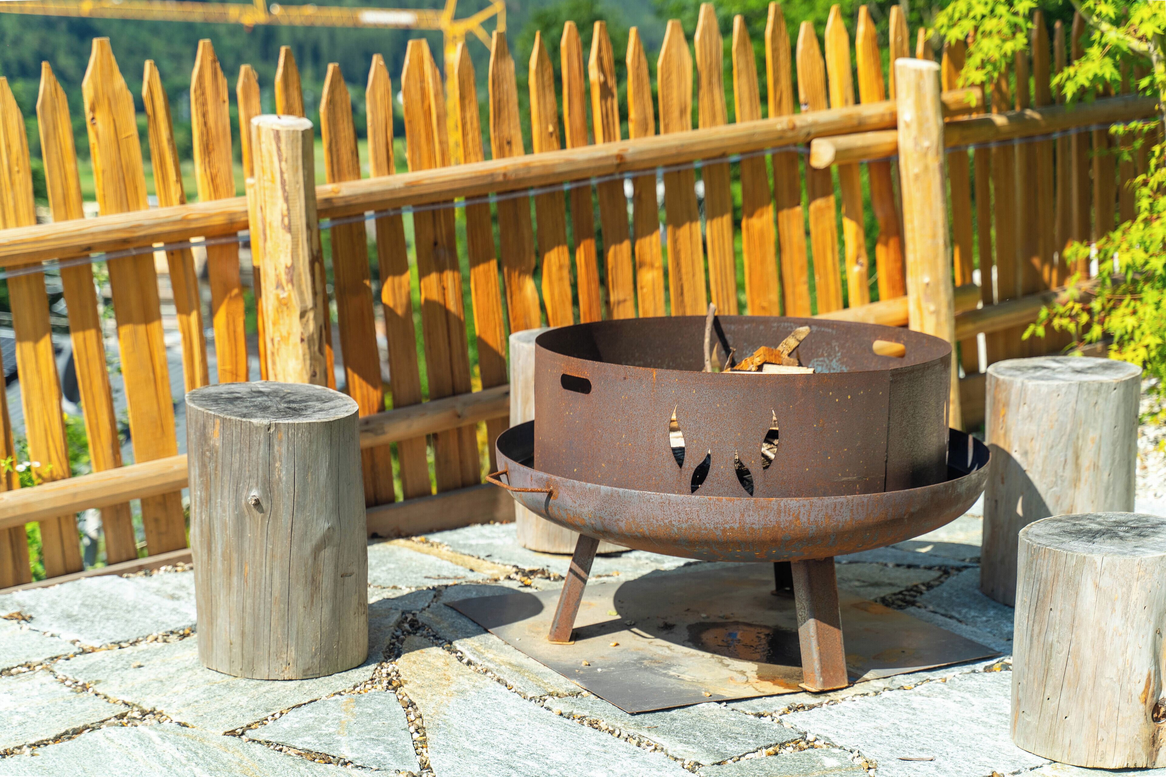 Eine Metall-Feuerstelle mit rustikalem Design, platziert auf einer Steinterrasse mit Holzstützen.