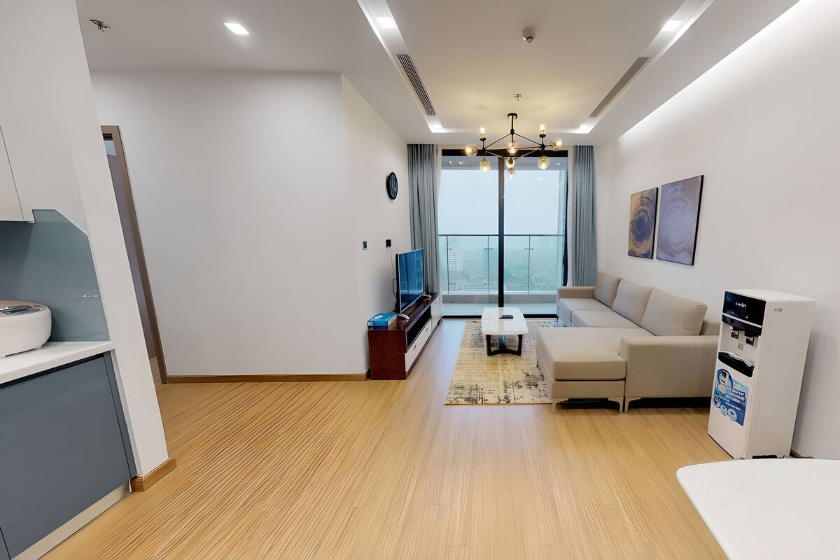 A modern living room with a sofa, coffee table, TV, and a view of the city through large windows.