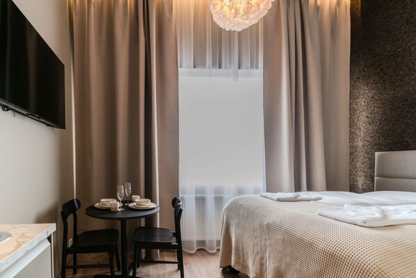 A hotel room with a bed, a small table with chairs, a TV mounted on the wall, and sheer curtains. - Frost Apartments - Economy Studio (Reykjavík)