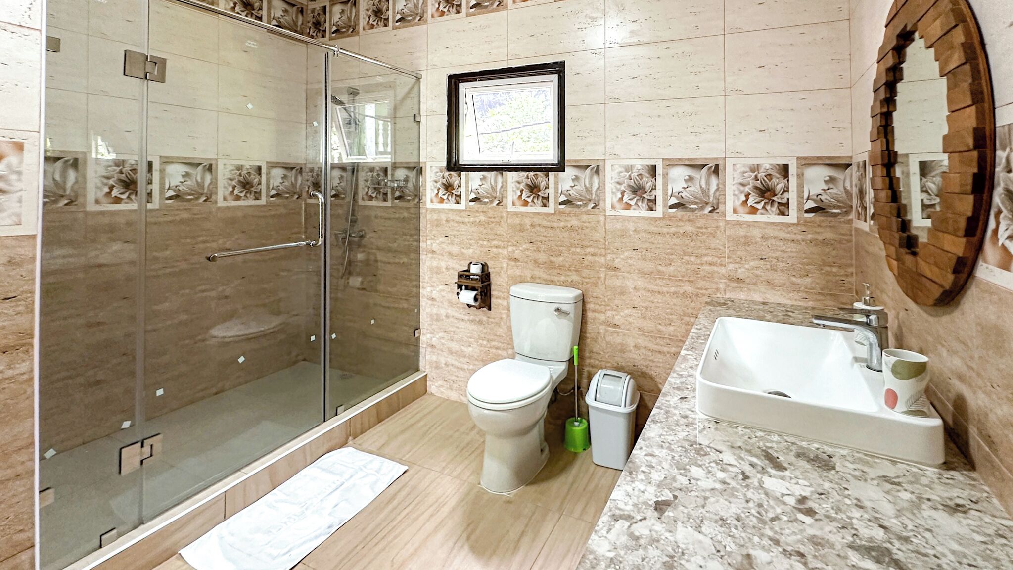 A bathroom with a glass shower enclosure, a toilet, a sink, and a framed picture on the wall.