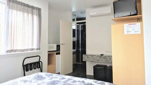 A hotel room with a bed, a TV on a shelf, a microwave, and a small kitchenette. - Studio Apartment in St Kilda next to Luna Park (St Kilda)