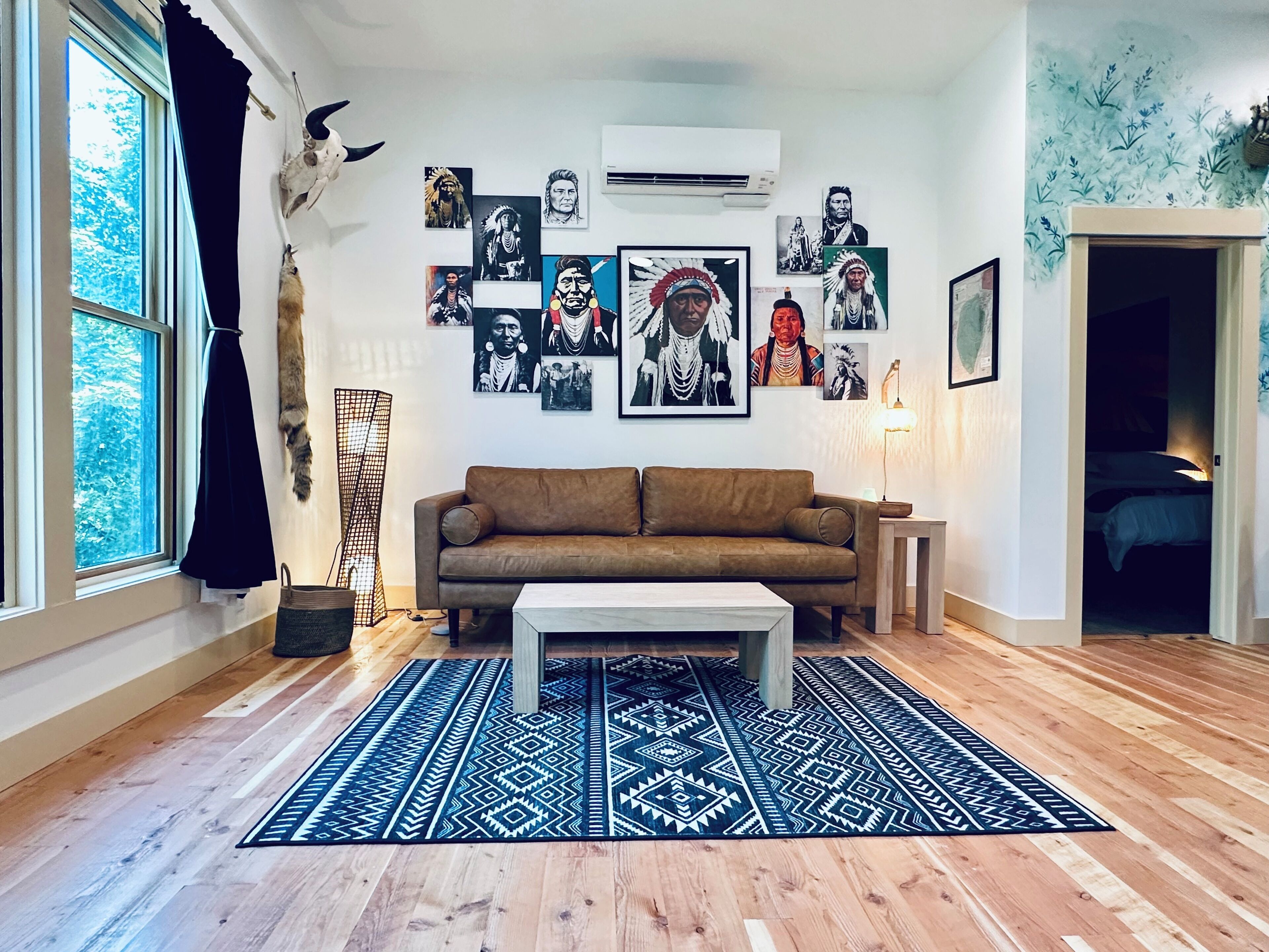 A living room with a brown sofa, a patterned rug, and various framed artworks on the wall.