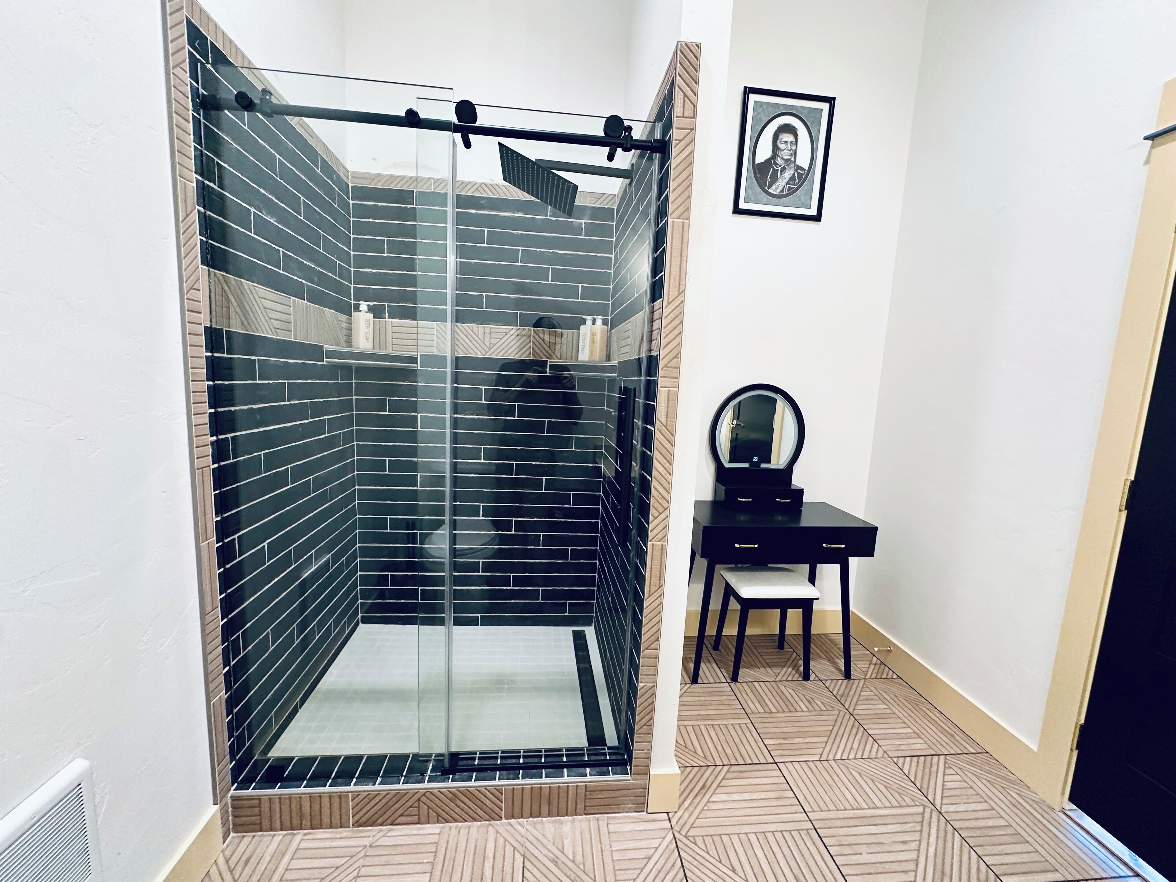 A bathroom with a glass-enclosed shower, a vanity with a mirror, and a framed picture on the wall.