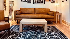Ein Wohnzimmer mit braunem Sofa, einem Couchtisch und einem gemusterten Teppich.