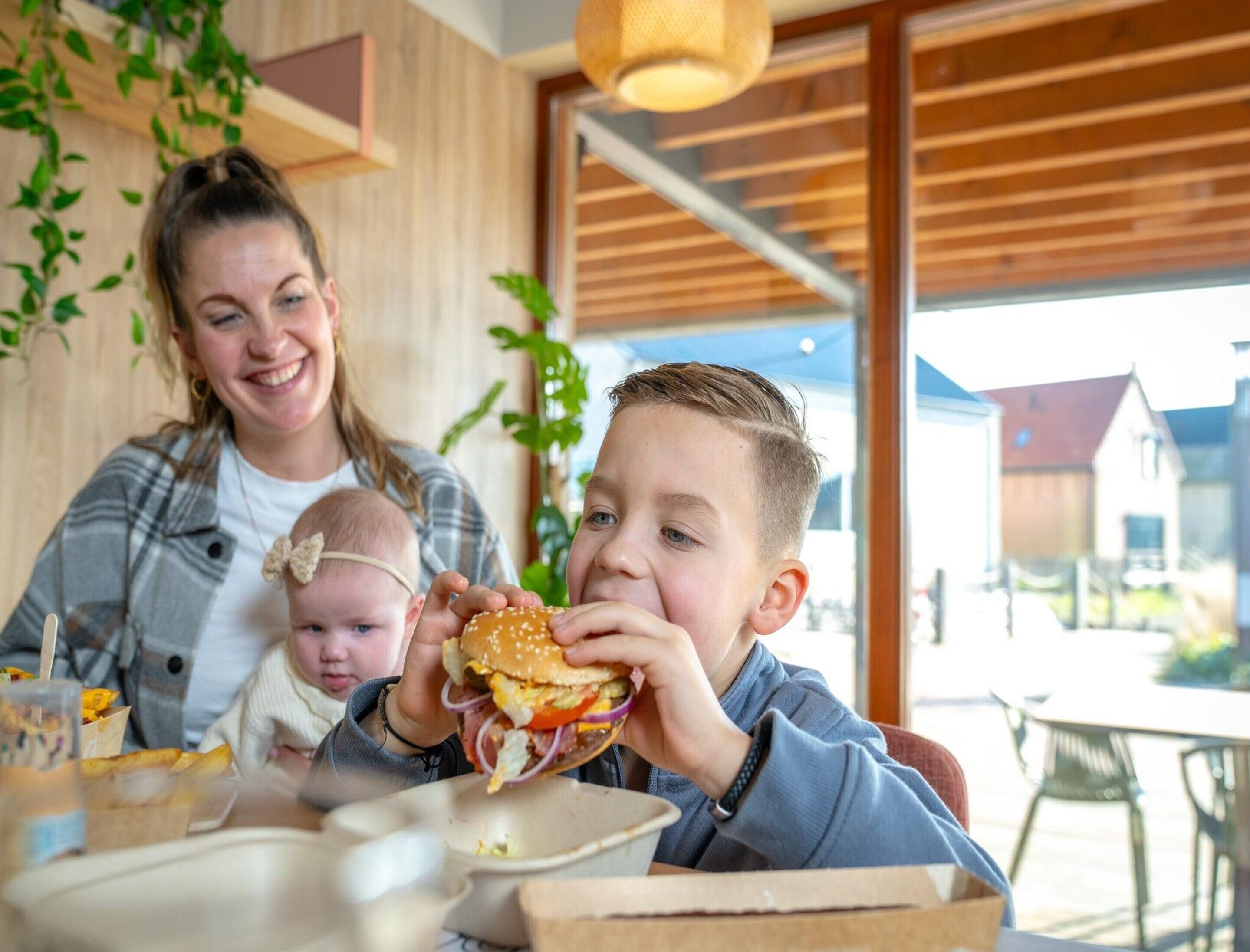 Eine Familie speist in einem Restaurant mit modernem Interieur, großen Fenstern und Blick nach außen.