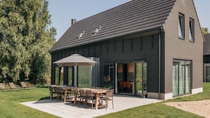 A modern house with a sloped roof, large glass doors, and a patio with outdoor furniture. - Villa by Lake Veere With Sauna (Wolphaartsdijk)