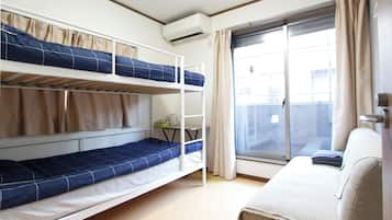 A dormitory room with bunk beds, a desk, and a window with curtains.