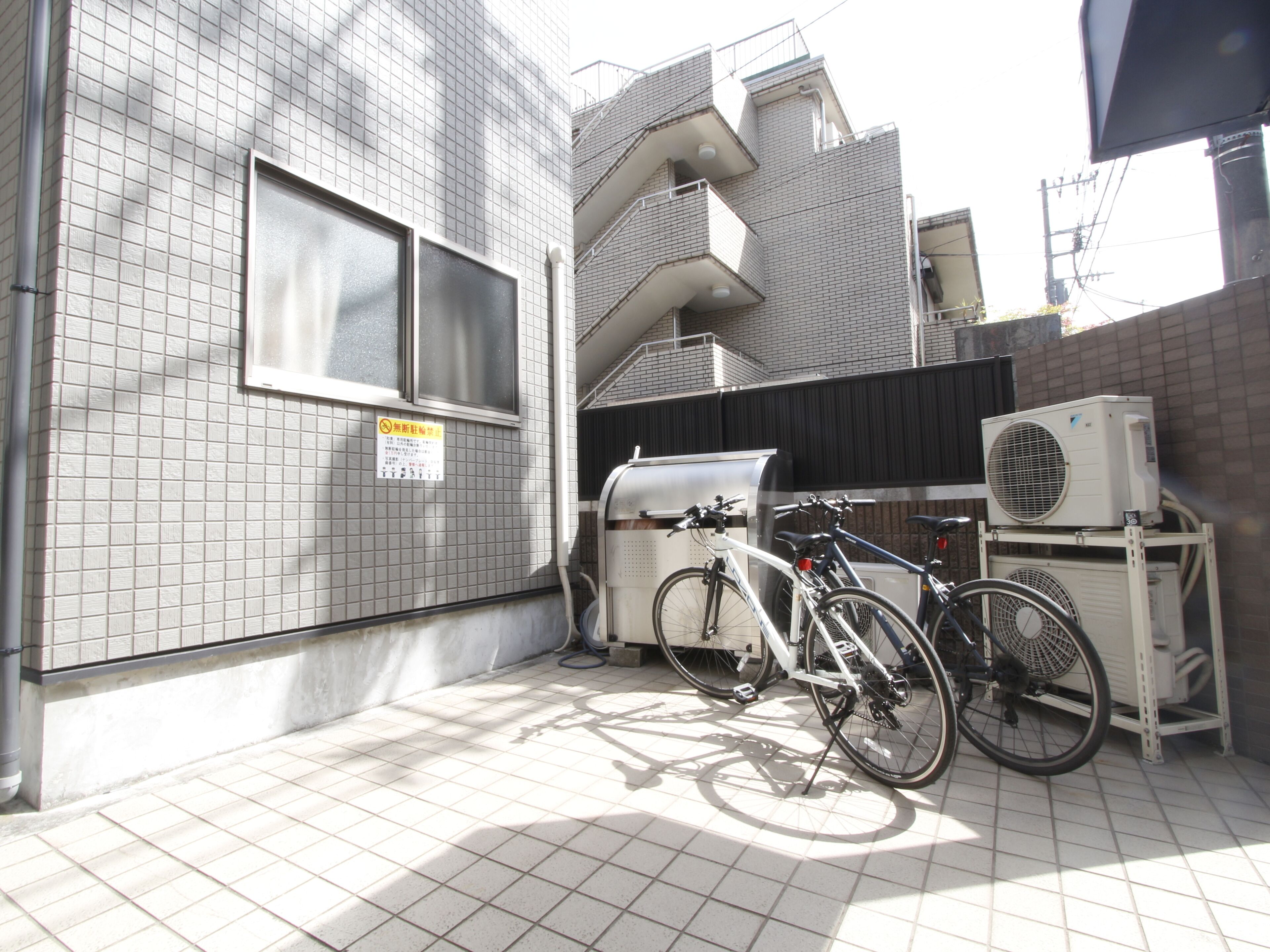 Un mur extérieur recouvert de carreaux, avec une fenêtre, un vélo et un appareil de climatisation.