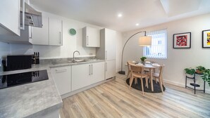 Una cocina moderna con armarios blancos, una placa de cocina de inducción negra y un comedor con una mesa redonda y sillas.