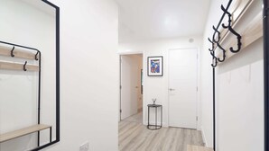 Un pasillo con un banco de madera, un perchero, una mesita con un cuadro y una puerta.