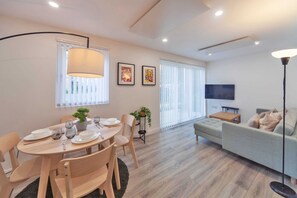 A modern living room with a dining area, featuring a sofa, TV, and a dining table set with plates and glasses. - Fantastic 2 Bedroom Apartment in Ashford (Ashford)