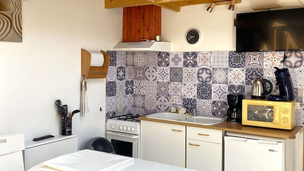 A compact kitchen with a stove, sink, and microwave. There's a wooden loft above the kitchen, and a dining table with chairs.