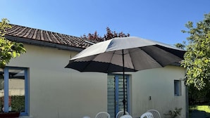 An outdoor patio with a table and chairs, a large umbrella, and a building with a tiled roof.