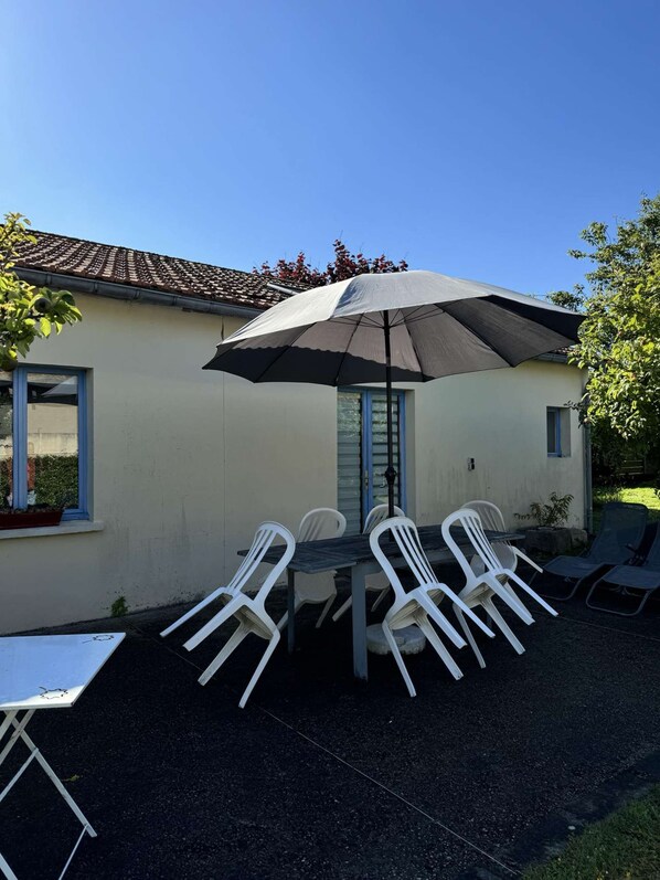 An outdoor patio with a table and chairs, a large umbrella, and a building with a tiled roof.