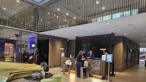 A modern hotel lobby with a reception desk, seating area, and a glass wall.