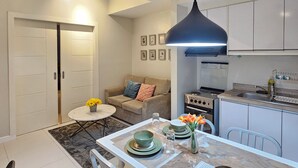 A modern kitchen with white cabinets, a dining table with a vase of flowers, and a sofa in the living area.