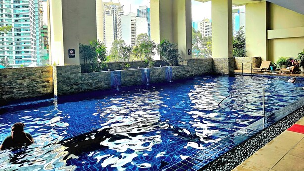 A swimming pool with a tiled floor, surrounded by stone walls and potted plants.