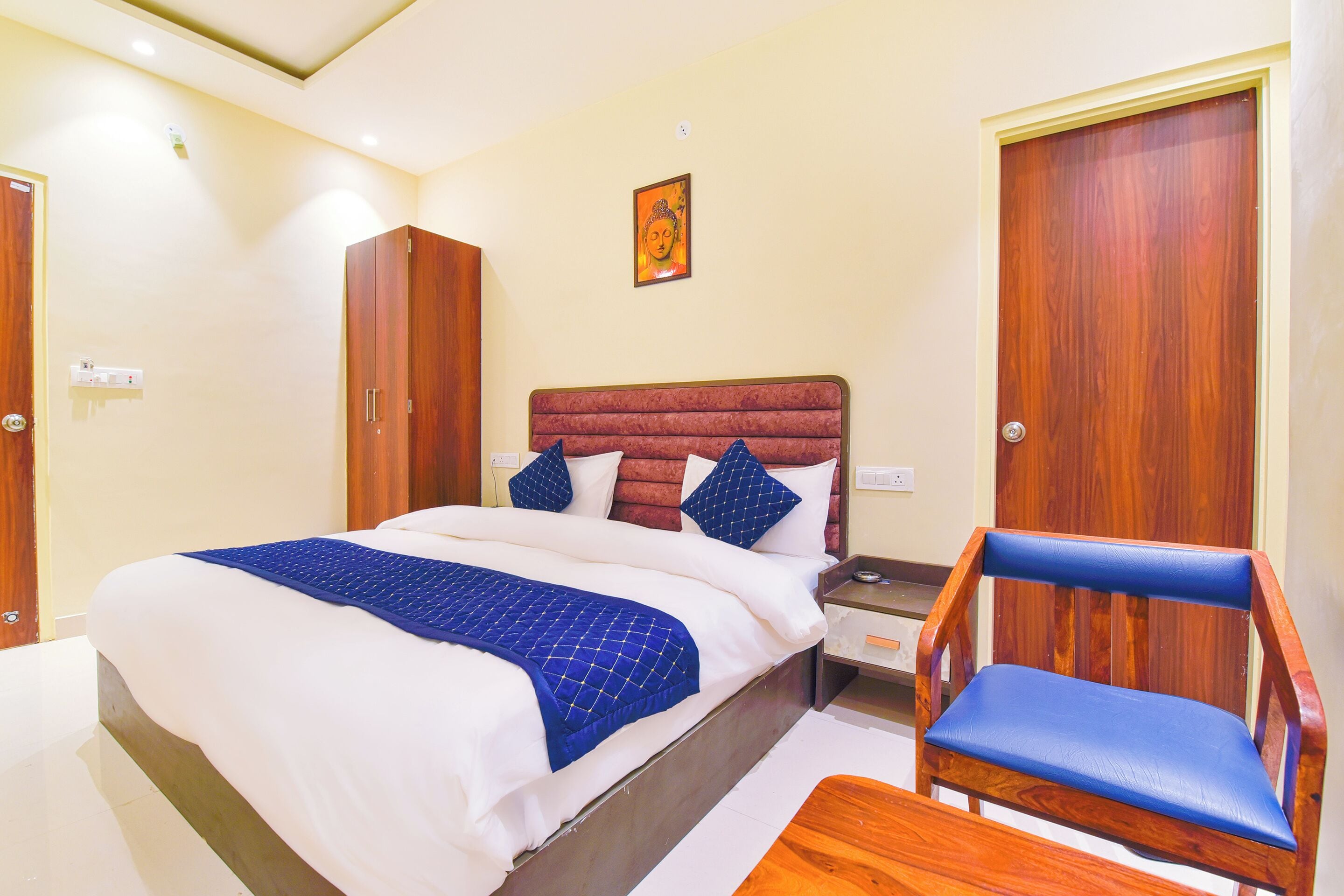 A neatly arranged hotel room with a bed, a wooden chair, a nightstand, and a wardrobe.