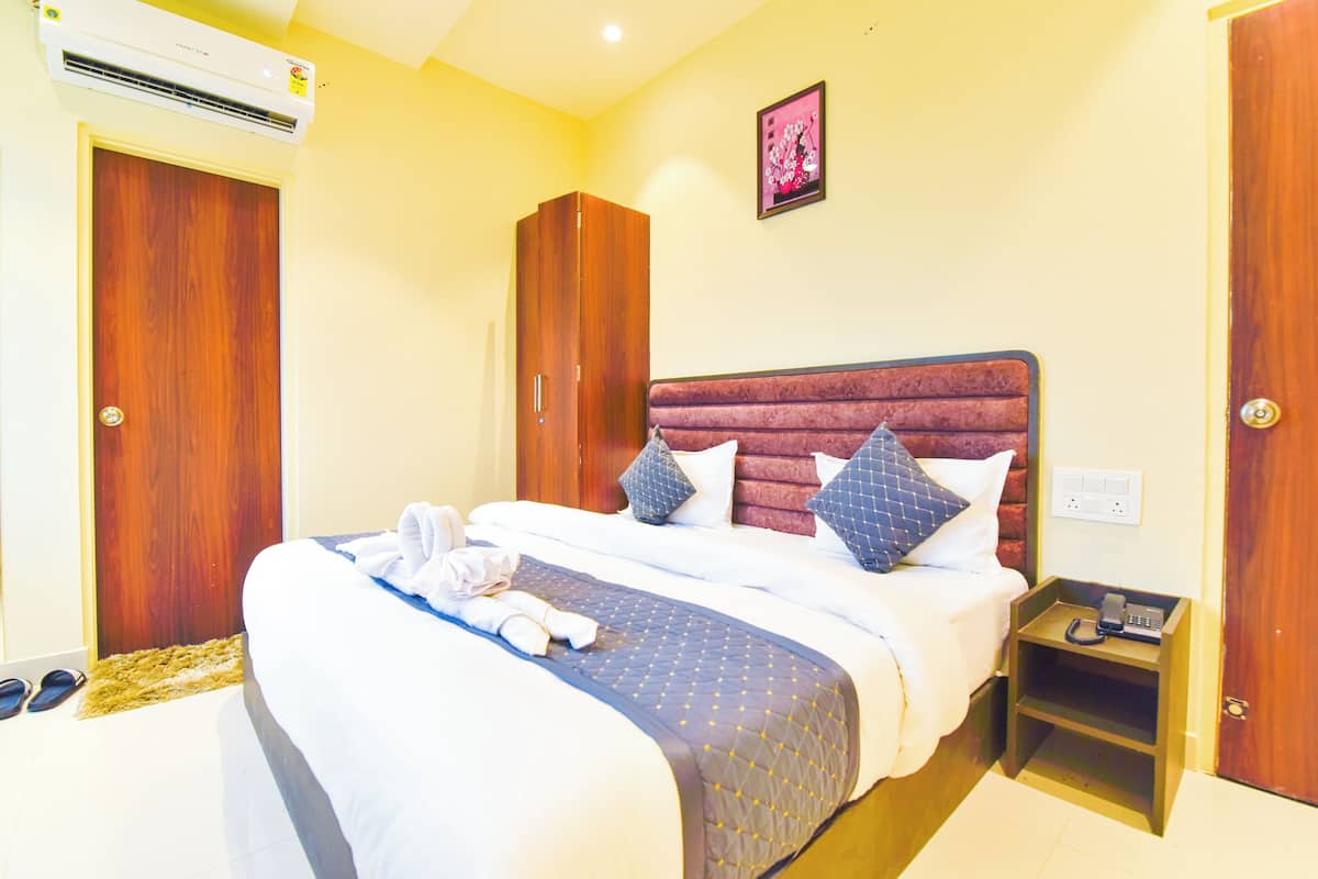 Una habitación de hotel con cama, mesita de noche, armario y equipo de aire acondicionado.