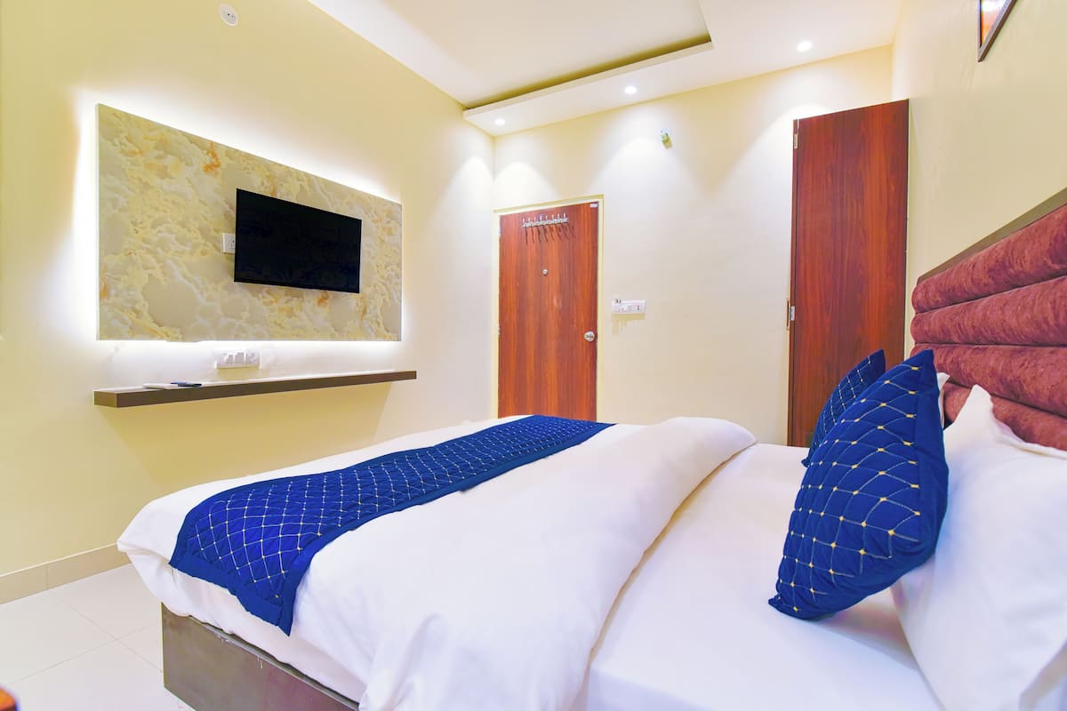 Habitación de hotel con cama, televisor montado, puerta de madera y cabecero rojo.
