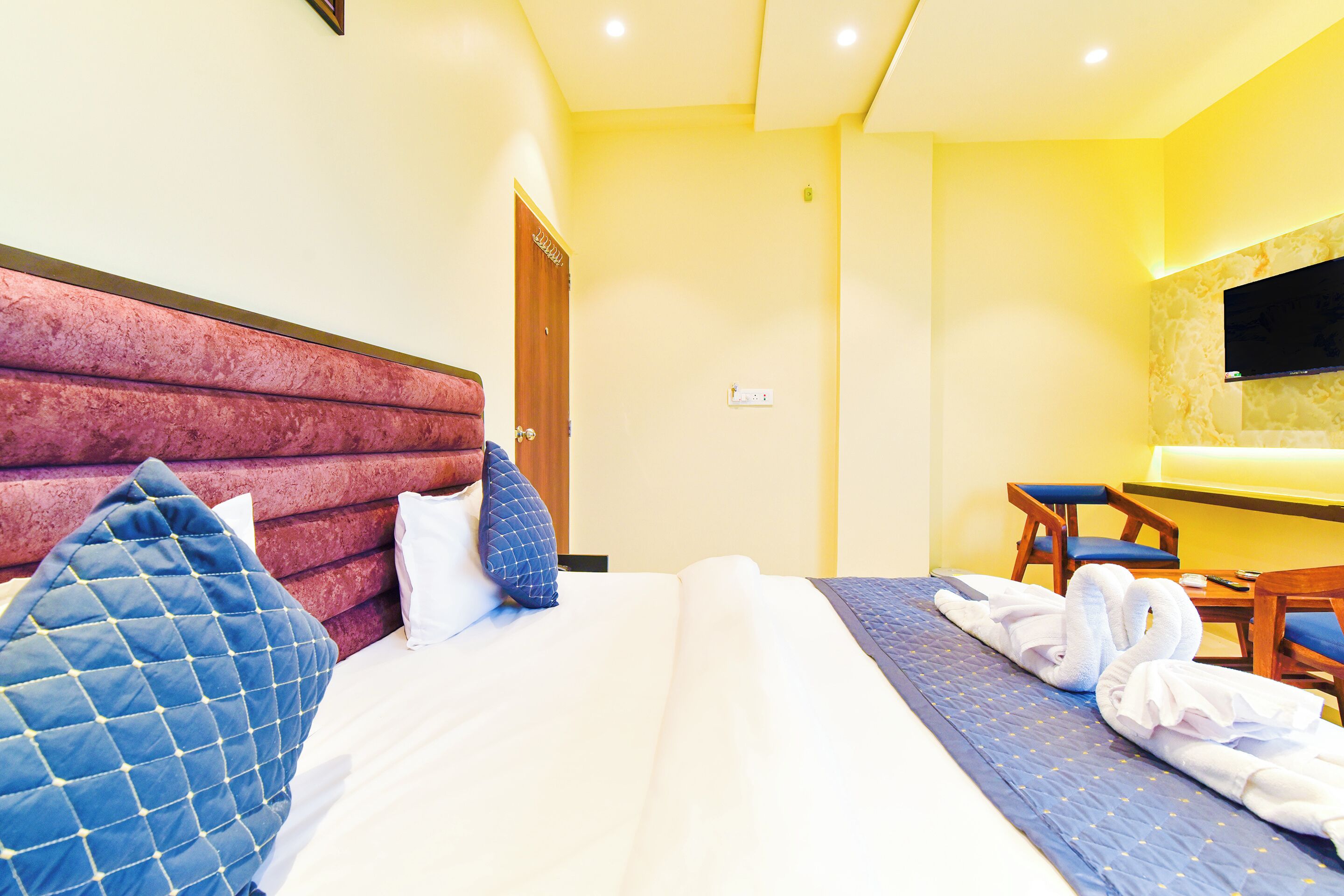 A hotel room with a bed, pillows, a desk, and a TV.