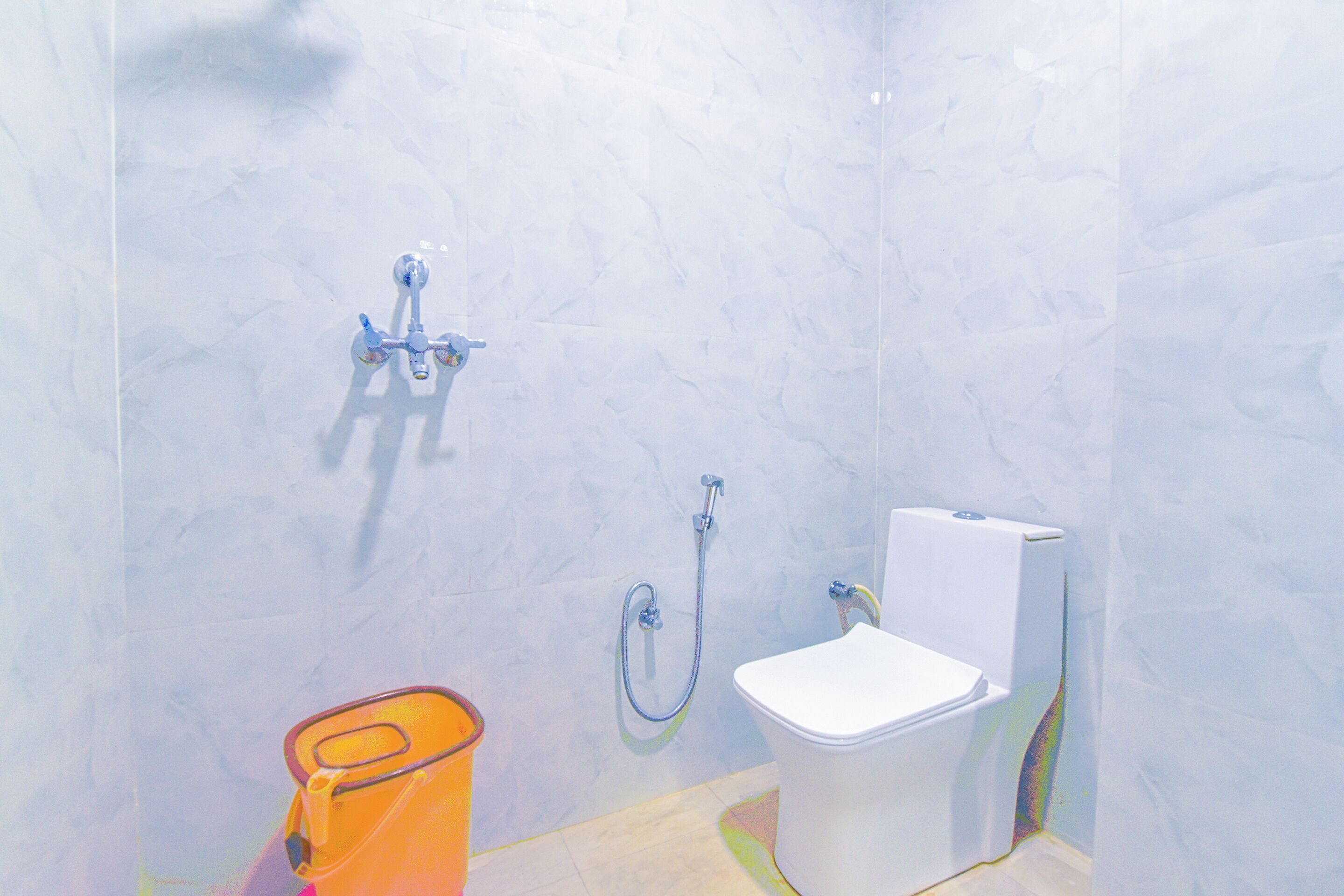 A bathroom with a white toilet, a shower, and a small orange trash bin.