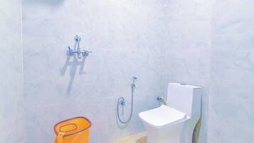 A bathroom with a white toilet, a shower, and a small orange trash bin.