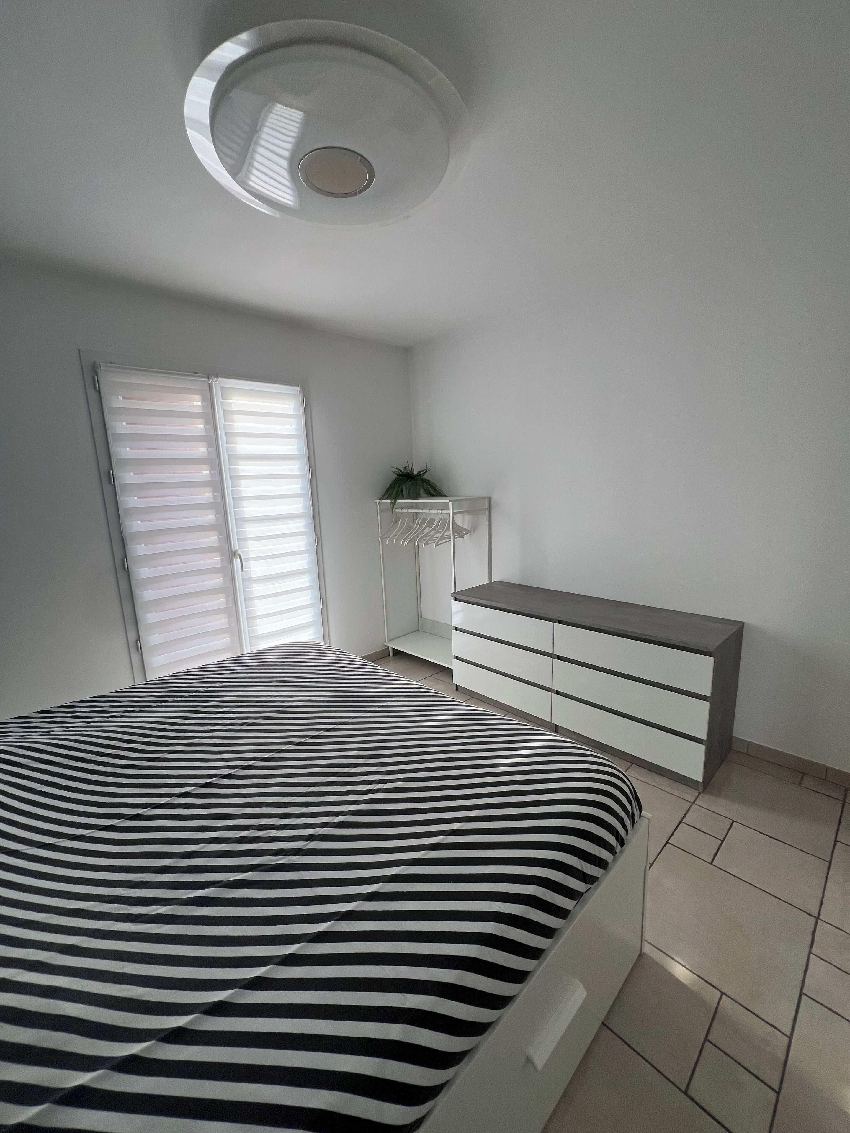 A bedroom with a bed, a dresser, a plant, and a ceiling light.