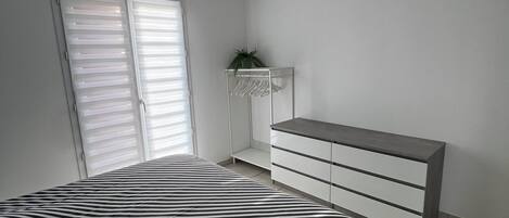 A bedroom with a bed, a dresser, a plant, and a ceiling light.