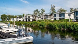 Ein modernes Wohngebiet mit Häusern entlang eines Kanals, wo Boote vertäut sind, und einem wolkenlosen Himmel.