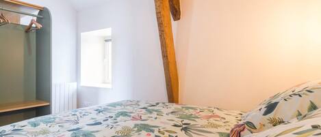 A bedroom with a floral bedspread, a wooden cross, a mirror, and a window.