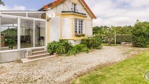 A house with a large glass door leading to a covered outdoor area, a satellite dish, and a garden with various plants and flowers. - Charming house with south-facing veranda and pets allowed (Le Vast)