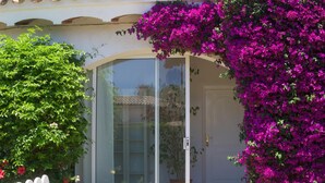 Une maison avec une porte-fenêtre coulissante, une clôture blanche en bois et un jardin orné de bougainvilliers violets.